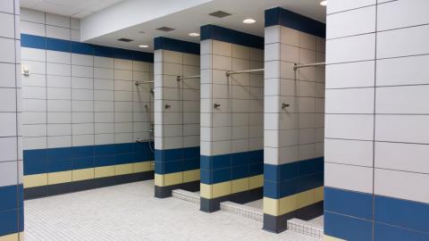 A row of showers in the tiled locker room, featuring extendable shower heads and ADA accessibility features.