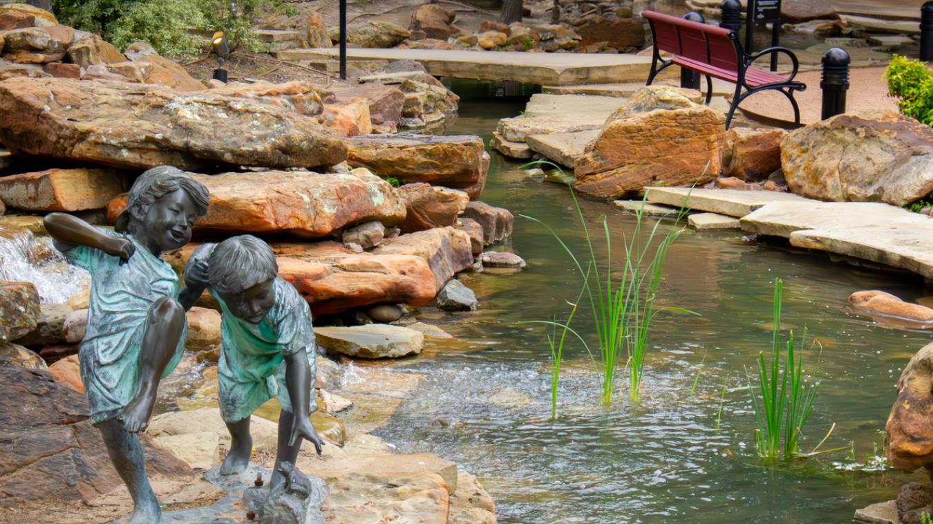 A statue of playing children sits on rocks beside a babbling brook at the Firewheel park.