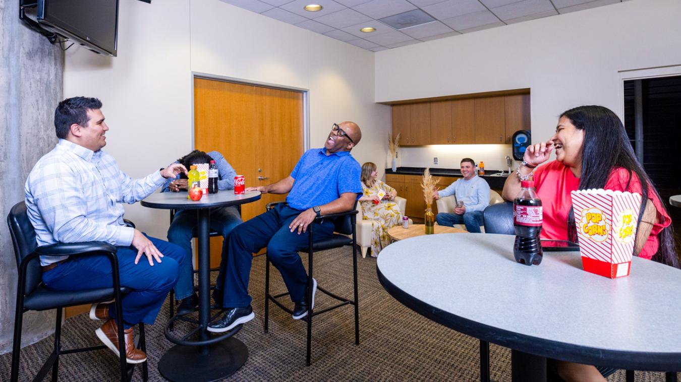 Laughing guests sitting at high top tables with refreshments in an arena suite.