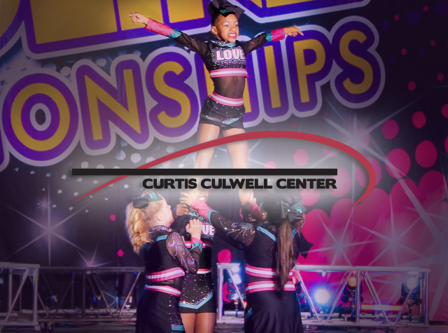 A group of young cheer leaders holds a different cheerleader in the air while she poses dramatically for a contest.