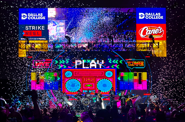 Fans dance excitedly as musicians perform and confetti falls, neon lights and a digital board illuminating them. Multiple CCC partners are featured on the digital board..